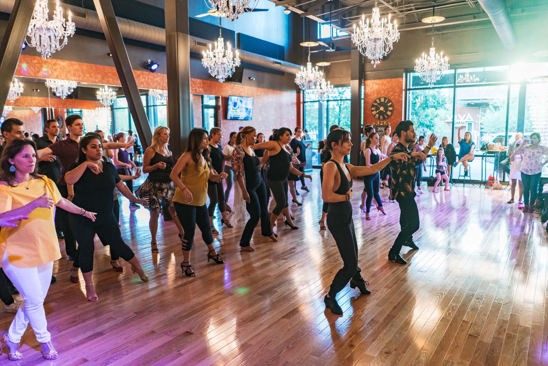Adults learning Latin dance steps together in a large group class at Dance With Me Austin