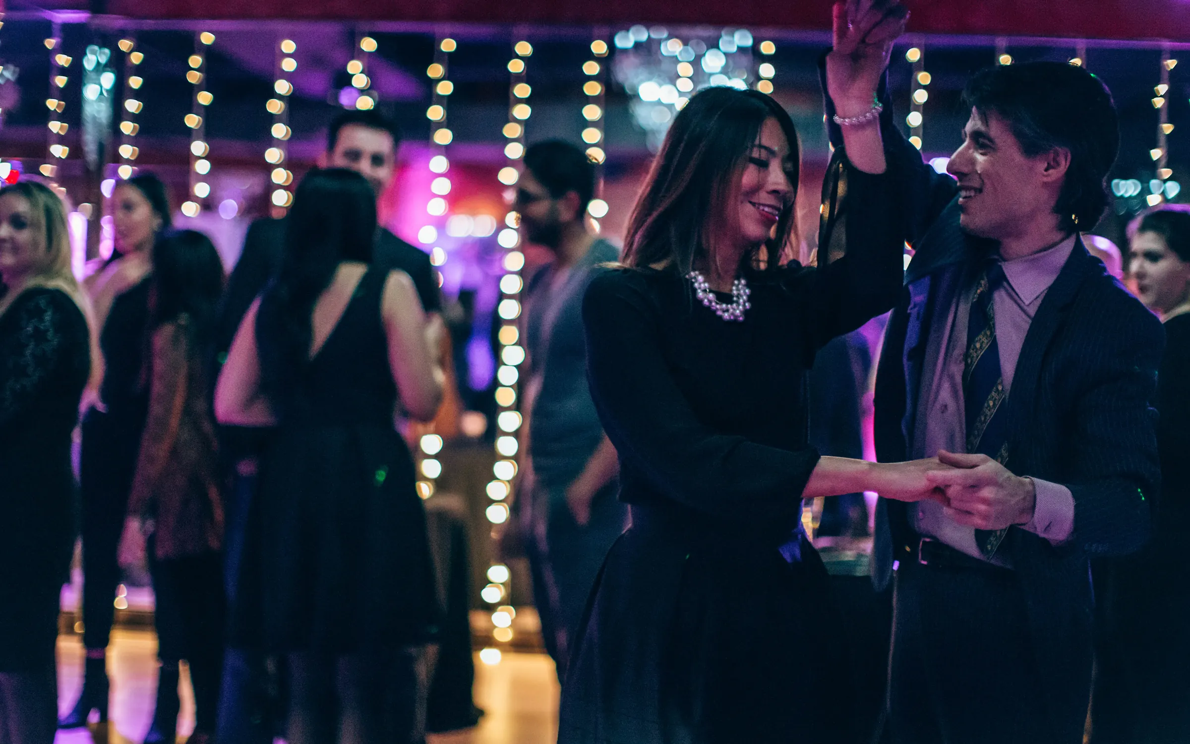 A smiling couple dancing salsa under string lights at a Dance With Me social party