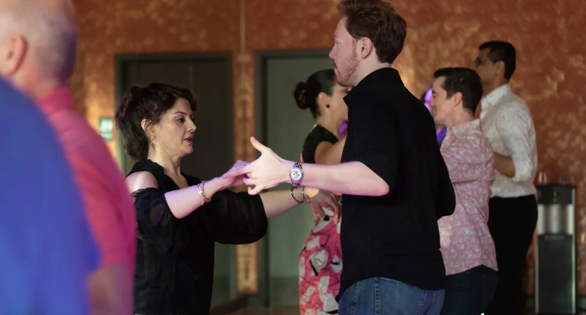 Couples practising a salsa hold together while partners rotate in a group class