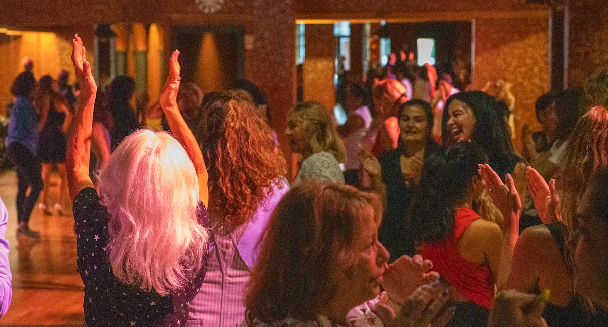Students clapping and dancing together on a crowded floor at a studio social party